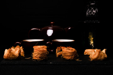 A low key and selective focus picture of Arabic baklava on slate plate with cup, teapot and lantern insight.