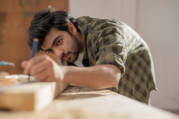 A YOUNG CARPENTER CAREFULLY MARKING MEASUREMENTS ON WOOD	