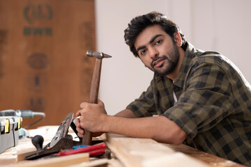 A CARPENTER HOLDING HAMMER   SITTING AND LOOKING AT CAMERA