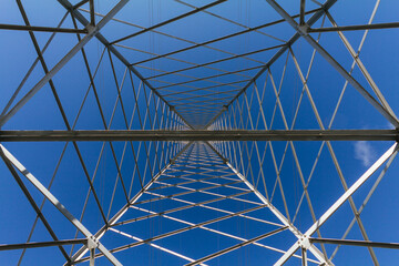 Low shot within a power transmission tower on a blue sky. Perfect symmetry