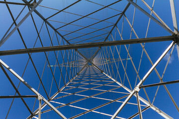 Low shot within a power transmission tower on a blue sky.