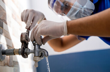 A PLUMBER WEARING FACE MASK AND SHIELD REPAIRING A LEAKING PIPE	
