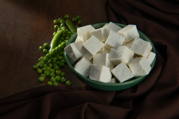 Diced Paneer in a green bowl with fresh raw peas 