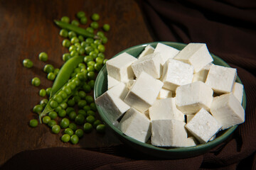 Diced Paneer or cottage cheese in a green bowl with raw peas 	
