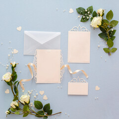 Mock up of invitation to wedding. Handmade greeting card. Frame from gentle white roses flowers on blue fabric background. Decorated background with artificial roses, beads and ribbons and card on it