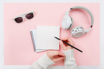 Top view mock up woman's hands with notebook, headphones, glasses on pink background. Copy space. 'To do' list. Planning of winter walk route, to-do list or shopping. Relax, wish list, play list