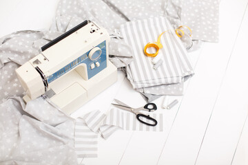 process of sewing of bed linen on sewing machine. Sewing kit. Grey fabric, scissors, threads, measuring tape and sewing machine on white wooden background