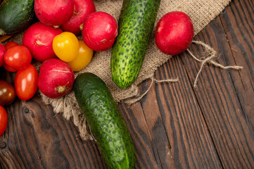 Green cucumbers, ripe radishes and colorful tomatoes scattered on the table. Close-up, selective focus.