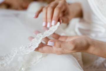 Fototapeta na wymiar Bride's hands with simple manicure touching lace veil or her wedding dress