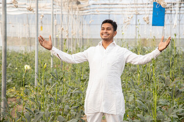 Young happy indian male farmer standing with open arms at his poly house or greenhouse, agriculture...