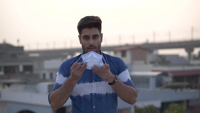 Hope, confidence-young man takes off his mask and smiling at camera.being tired of wearing the mask - young man takes off his mask sighing.Man is relieved to remove mask off his face during covid-19 .