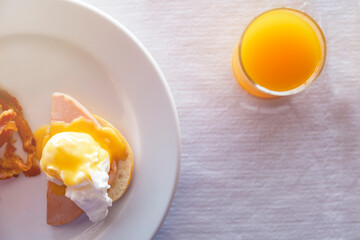 Top view close up orange juice in glass and egg benedict breakfast on white Tablecloth. food and drink concept.Top view breakfast with poached eggs royale