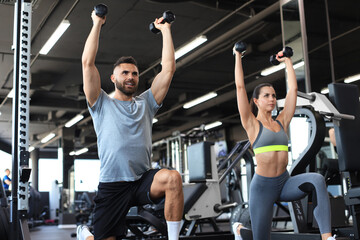 Attractive sports people are working out with dumbbells at gym.
