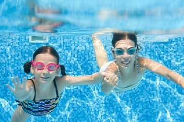 Children swim in swimming pool underwater, little active girls have fun under water, kids fitness and sport on active family vacation
