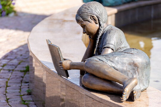 Russia Zlatoust August 2020: bronze sculpture of a girl lying on a bench reading a book in the P.P. Bazhova on a summer day.