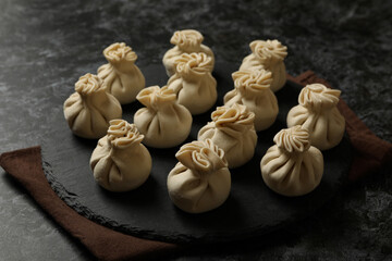 Tray with raw khinkali on kitchen towel on black smokey background