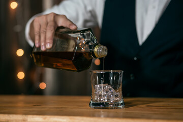 Waitress man standing pours whiskey into a glass