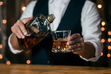 Waitress man standing pours whiskey into a glass