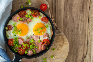 Fried eggs with sausages, tomatoes and vegetables.