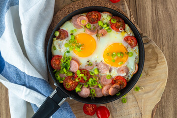 Fried eggs with sausages, tomatoes and vegetables.