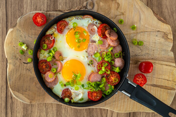 Fried eggs with sausages, tomatoes and vegetables.