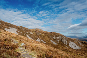 Fototapeta premium View from Diamond hill in Connemara National park, county Galway, Ireland, Small walking path. Bright sunny day, blue cloudy sky. Mountains in the background