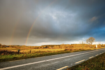 Double rainbow over country side and small asphalt road, West of Ireland. Fall and winter season. Blue cloudy sky