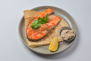 Grilled salmon steak served on a lavash bread with a piece of lemon and sauce.