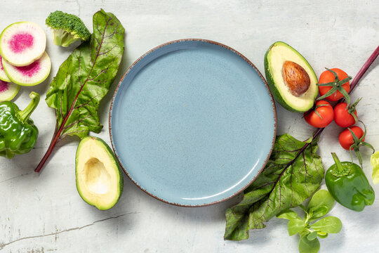 Fresh vegetables on gray background an empty plate in center. Top view