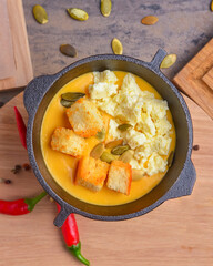 Pumpkin soup served in a bowl over wooden background with spices. Autumn seasonal meal.