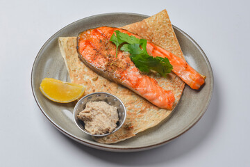 Grilled salmon steak served on a lavash bread with a piece of lemon and sauce.