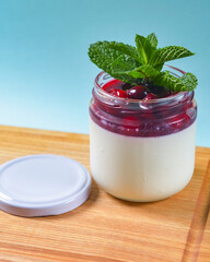 Italian dessert panna cotta with fresh berries and mint leaf on top. Served in a small glass on a rustic wooden board.