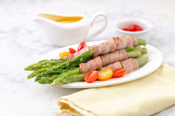 Fried green asparagus wrapped in bacon with hollandaise sauce and fresh cherry tomatoes.