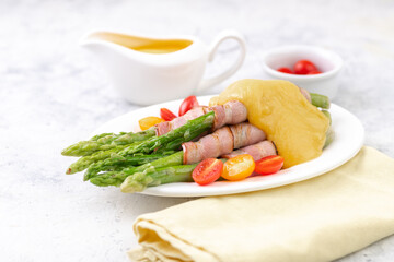 Fried green asparagus wrapped in bacon with hollandaise sauce and fresh cherry tomatoes.