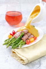 Fried green asparagus wrapped in bacon with hollandaise sauce and fresh cherry tomatoes.