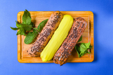 Different coloured eclairs on a wooden board over blue background. French dessert concept, French...