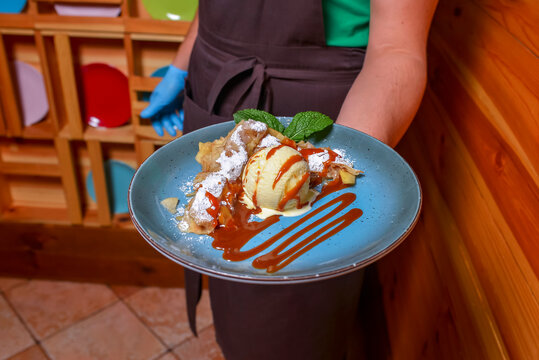 Waiter serving ice cream dessert in restaurant or diner. Eating out concept. Apple pie with ice cream and caramel sauce.
