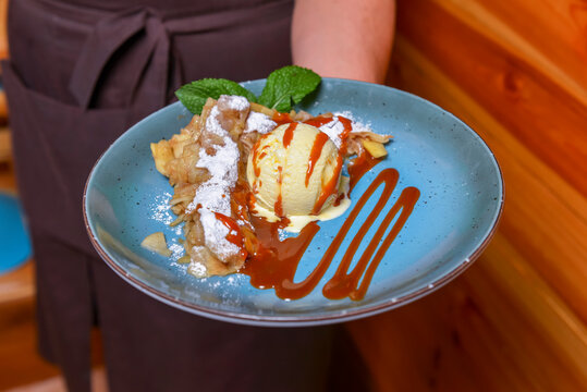 Waiter serving ice cream dessert in restaurant or diner. Eating out concept. Apple pie with ice cream and caramel sauce.