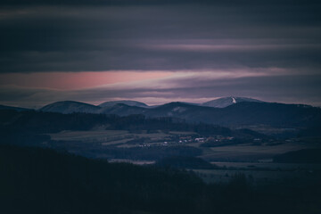 Sunset dark sky with clouds over the mountainous landscape of Pustevny lying under the fog in a dark color.