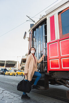 Beautiful girl wearing protective medical mask and fashionable clothes poses with red tram at istiklal street in Istanbul,Turkey. New normal lifestyle concept.
