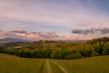 Naklejka na ściany i meble Landscape full of hills and mountains with clouds and blue sky with sun during colorful sunset Beskydy region.