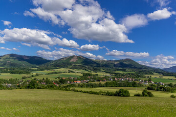 Fototapeta na wymiar Ondrejnik and views of other Beskydy hills and mountains with white clouds and blue sky in the background during a sunny day.