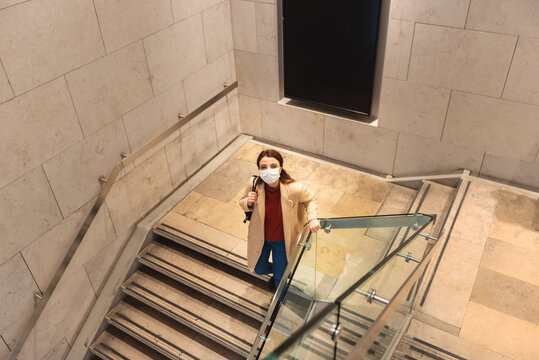 Beautiful girl wearing protective disposable mask and fashionable clothes walking down at stairs. New normal lifestyle concept.