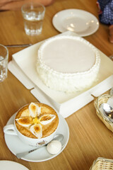Coffee decorated with baked marshmallows in the shape of a flower stands next to a large white cake. cake concept for lettering