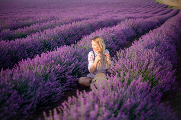 Portrait of beautiful blond woman with long curl hair relax in the purple field with lavender flowers. Woman walking in the sunrise and breathes the scent of Provencal herbs