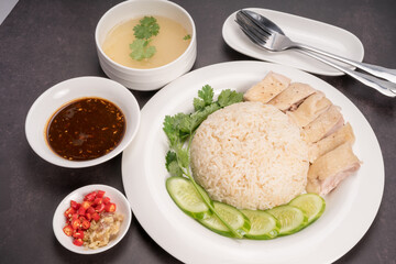 Hainanese chicken rice. Roasted Chicken Rice with soup, vegetable and Garlic, chili, ginger sauce on gray background.