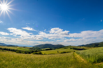 Fototapeta premium Ondrejnik and views of other Beskydy hills and mountains with white clouds and blue sky in the background during a sunny day.