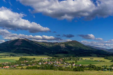 Fototapeta na wymiar Under the sun and shadows Ondřejník and a view of other Beskydy hills and mountains with white clouds and blue sky in the background.
