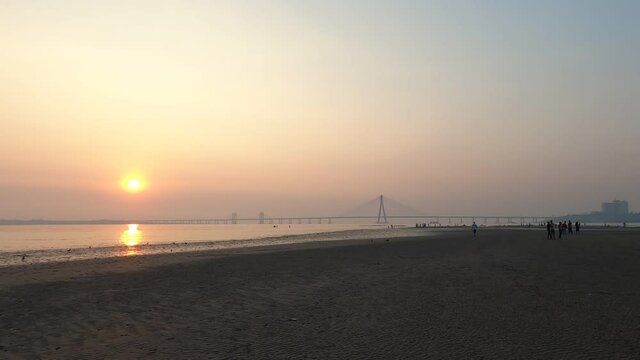 4K Real Time Wide Angle footage of Mumbai's Bandra Worli Sea Link Bridge (BWSL) on a smoggy hazy evening during sunset. Dadar beach, Mumbai, Maharashtra, India. GH010732.