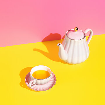 Teapot with cup of tea on multi colored pink and yellow background. Minimal herbal organic beverage concept. Trend shadows.
